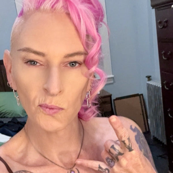 Person with pink hair and tattoos in a room setting